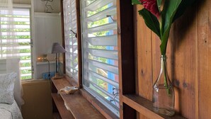 Ein Zimmer mit Holzwänden, einer Bank, einem Nachttisch mit Lampe und einem Fenster mit Blick auf Grünflächen.