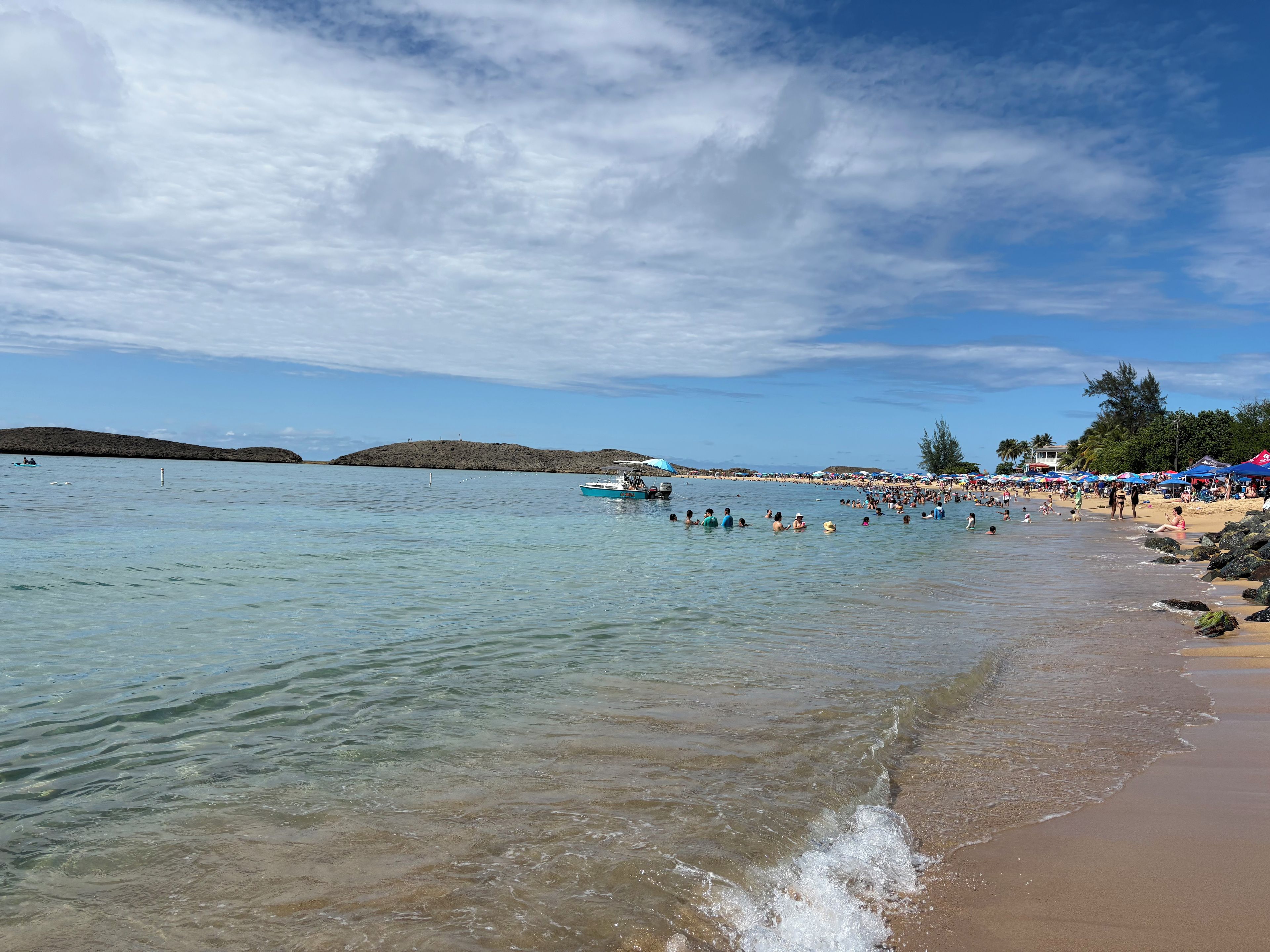 Una playa con agua cristalina, un bote y gente nadando.