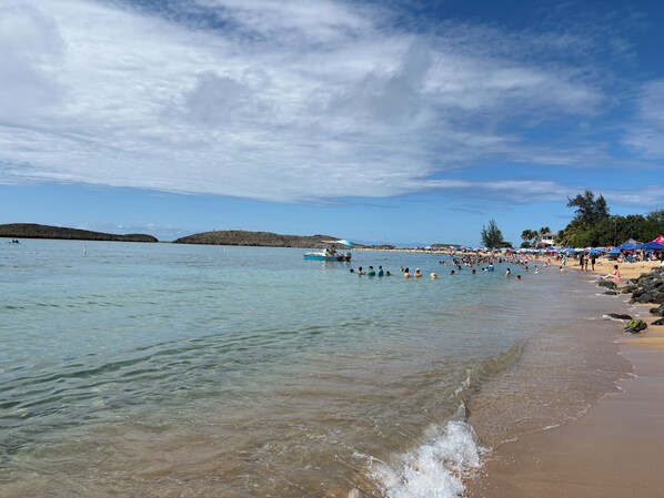 A beach with clear water, a boat, and people swimming.
