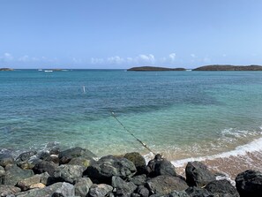 A rocky shoreline with clear turquoise water and distant islands.
