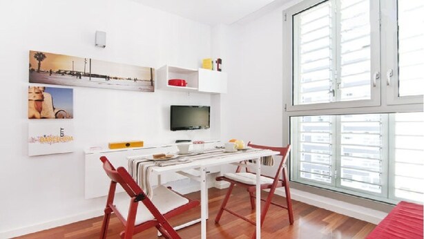 A bright room with a dining table, chairs, a TV, and a window with blinds.