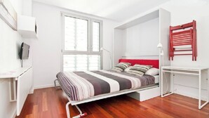 A modern bedroom with a bed, a desk, and a TV.