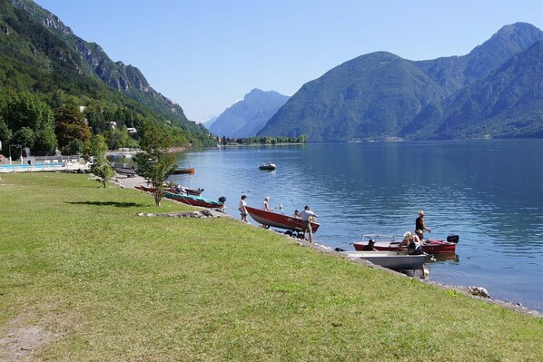 A lakeside view with boats docked, grassy areas, and mountains in the background. - Directly on the lake with fenced garden (Tre Capitelli)