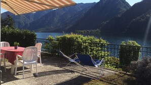 A terrace with a table and chairs, overlooking a lake and mountains. - Directly on the lake with fenced garden (Tre Capitelli)
