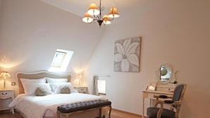 A bedroom with a bed, bedside lamps, a desk with a chair, a mirror, and a flower painting on the wall. - Charming historic cottage, 5 bedrooms, large garden (Coulonges-sur-Sarthe)