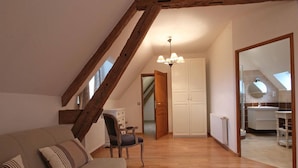A cozy loft bedroom with a sloped ceiling, a wooden beam structure, a bed, a chair, and a wardrobe. - Charming historic cottage, 5 bedrooms, large garden (Coulonges-sur-Sarthe)