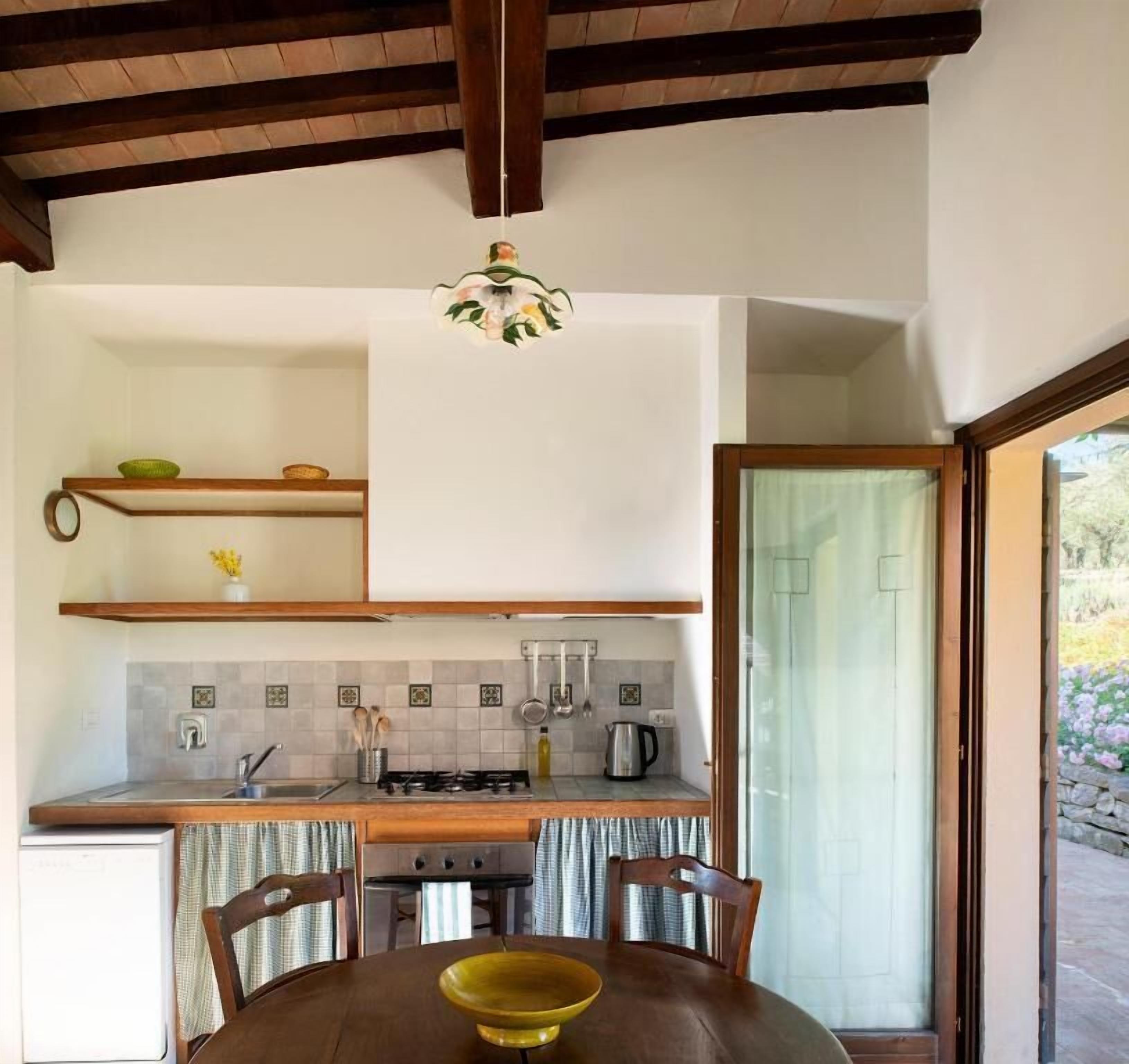 A compact kitchen with a dining area, wooden ceiling beams, and a view through a glass door.