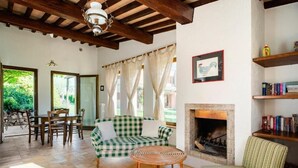 A cozy living room with a checkered sofa, a round wicker table, and a striped armchair. A fireplace is visible in the background, and there are bookshelves with books. - Ginestra (Montefalco)