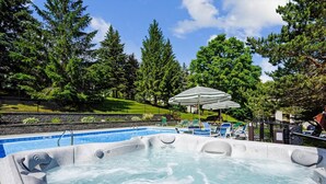 Un jacuzzi rodeado por una piscina, con sillas de descanso y una sombrilla.