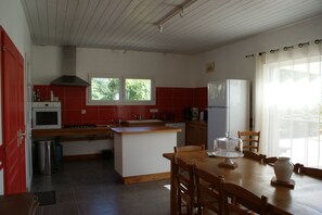 Una cocina con una isla central, estufa, pileta y refrigerador. Hay ventanas que dejan entrar luz natural y ofrecen vistas a la vegetación.