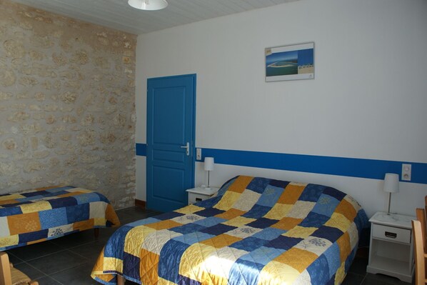 A room with two beds, a blue door, a small painting, and a white wall.