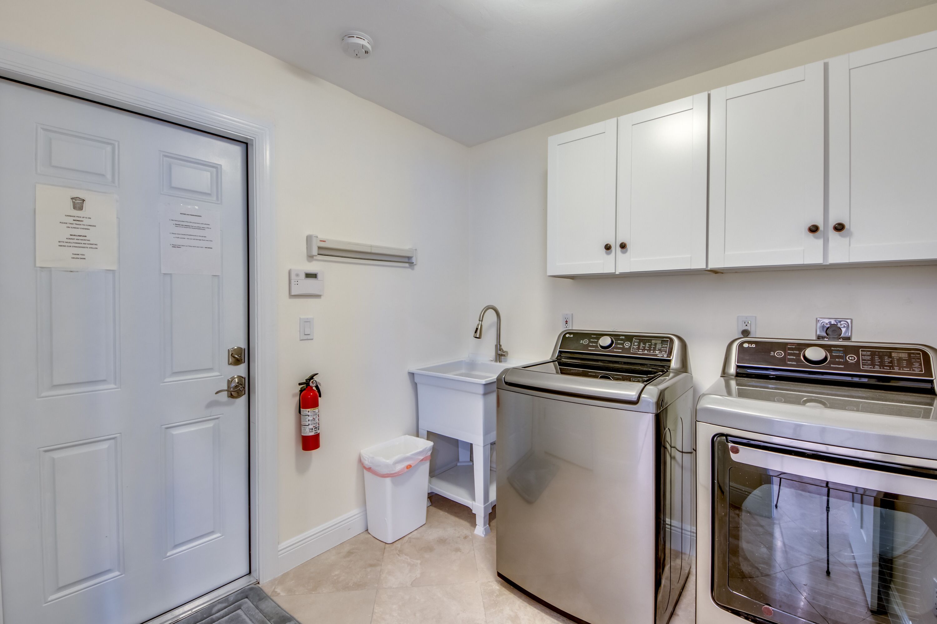 A laundry room with a washing machine, dryer, and a small sink with a trash can.