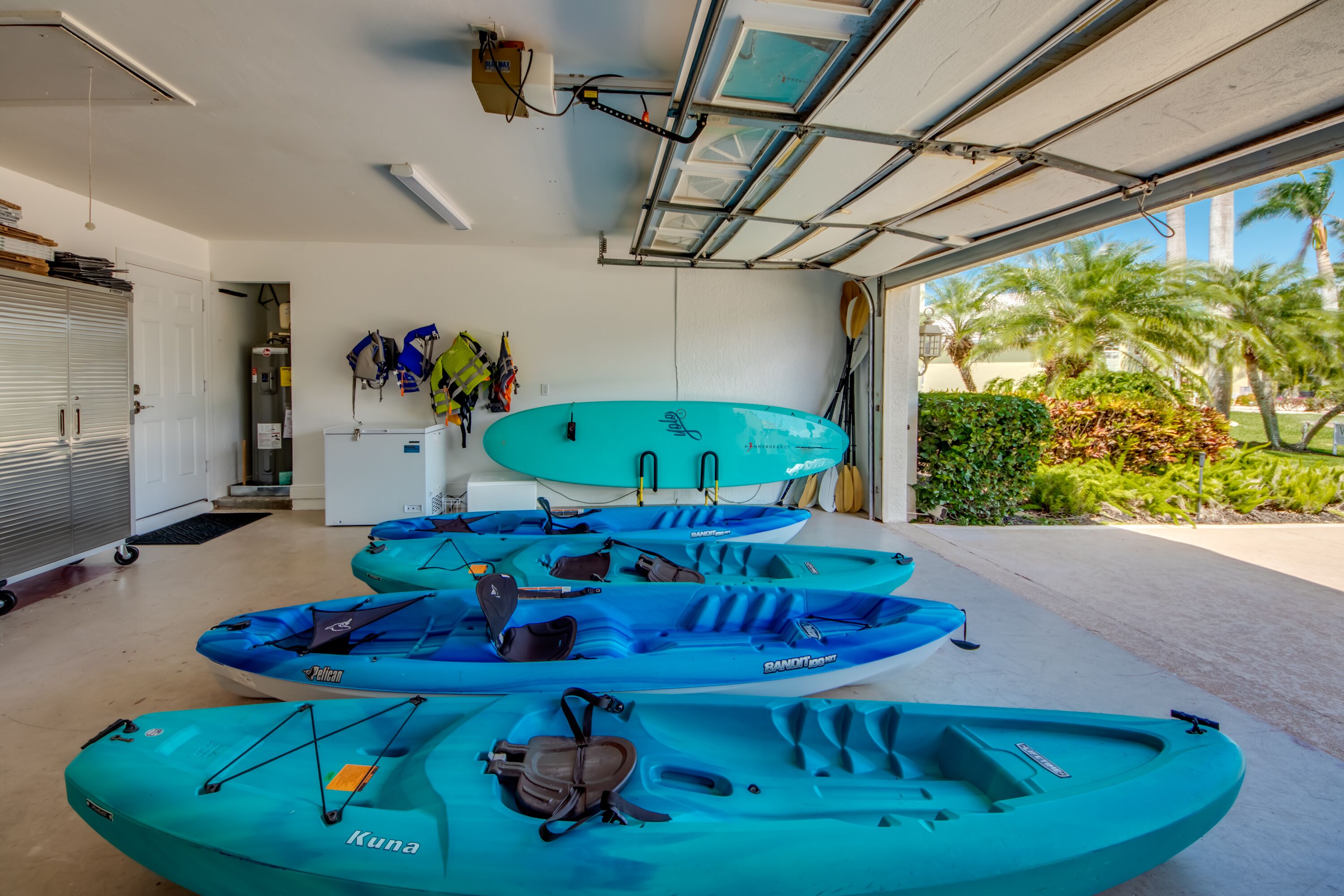 A garage with kayaks and a canoe, a white door, and a view of palm trees.