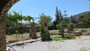 Une cour extérieure aux murs de pierre, sous un ciel d’un bleu éclatant, agrémentée de quelques plantes.