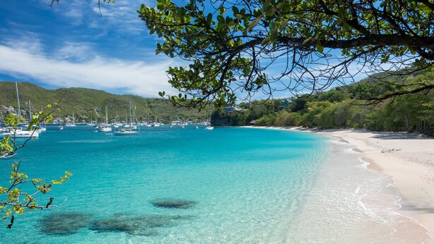 En strand med krystalklart turkis vand, både og en sandet kyst.