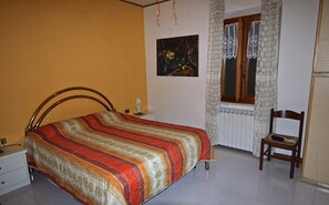A bedroom with a bed, a chair, a nightstand, a painting, and a window with curtains. - The Tower in Solebello (Morro D' Alba)