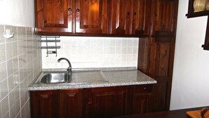 Cuina amb armaris de fusta, un rentaplat de stainless steel i una barra de resguard rebedor de rajoles.