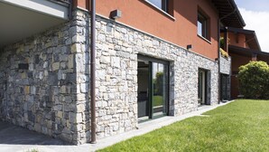 Un bâtiment moderne avec une façade en pierre, de grandes portes vitrées et une pelouse bien entretenue.