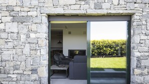 Un intérieur moderne avec des murs en pierre, une porte-fenêtre coulissante donnant sur un jardin et un coin salon avec un canapé et une table.