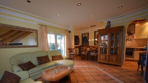 Un salon comprenant un canapé, des fauteuils, une table à manger et un coin cuisine avec des placards et une cuisinière.