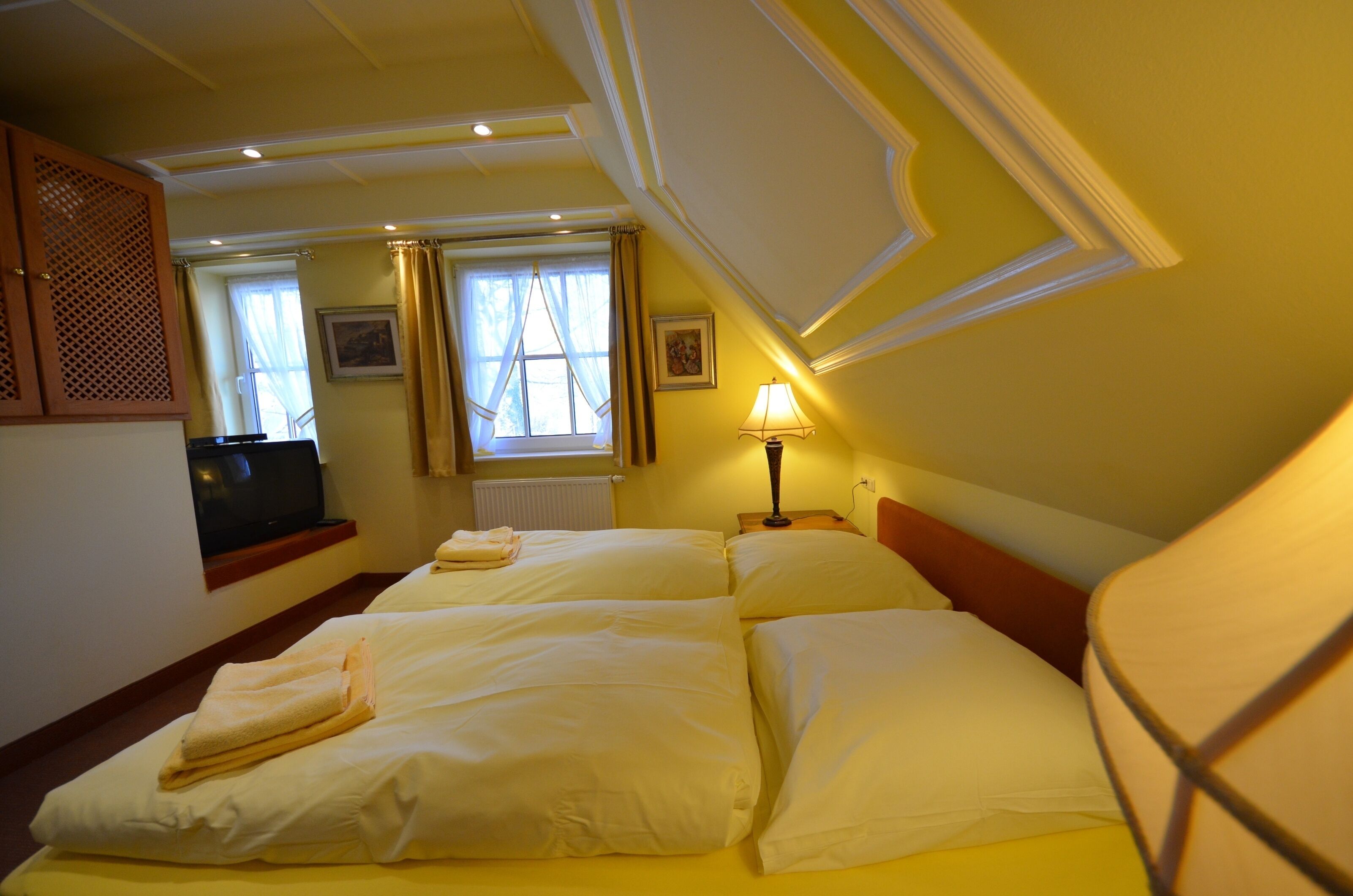 A hotel room with two beds, a television, a window with curtains, and a lamp.