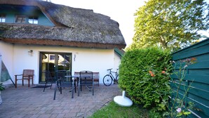 Une maison à toit de chaume avec un patio dallé, des sièges d’extérieur et un vélo.