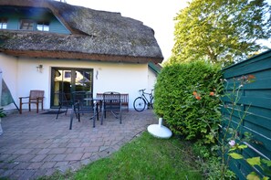 Een rieten huis met een geplaveid terras, zitplaatsen buiten en een fiets.