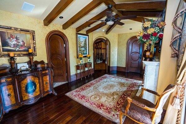 A spacious foyer with wooden flooring, a large ornate rug, and a ceiling fan.