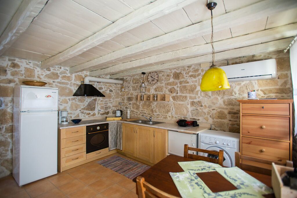 A compact kitchen with a stone wall, wooden cabinets, a white refrigerator, a sink, a stove, and a yellow pendant light.