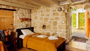 Ein rustikales Schlafzimmer mit Steinsandsteinwänden, einem hölzernen Bett, einem kleinen Bücherregal und Blick ins Grüne.