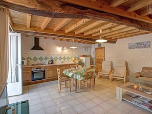 A kitchen with wooden beams, a dining area with a table and chairs, and a living room with a sofa and a coffee table.
