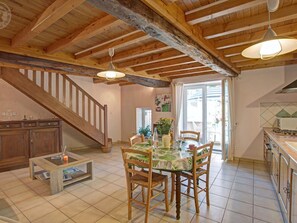 A spacious kitchen with wooden beams, a dining area with a table and chairs, and a staircase leading to another level.
