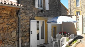 Un edificio de piedra con una puerta, un espacio de estar al aire libre techado con sillas y un pequeño jardín.