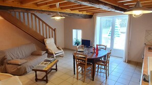Una sala de estar acogedora con una escalera de madera, una mesa de comedor preparada para cuatro personas y un ventanal que proporciona luz natural.