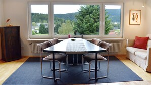 Ein Essbereich mit Tisch und Stühlen, einem Heizkörper und einem Fenster mit Blick auf Bäume und Gebäude.