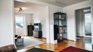 Ein Wohnzimmer mit Fernseher, Bücherregal und einem Essbereich mit Tisch und Stühlen.