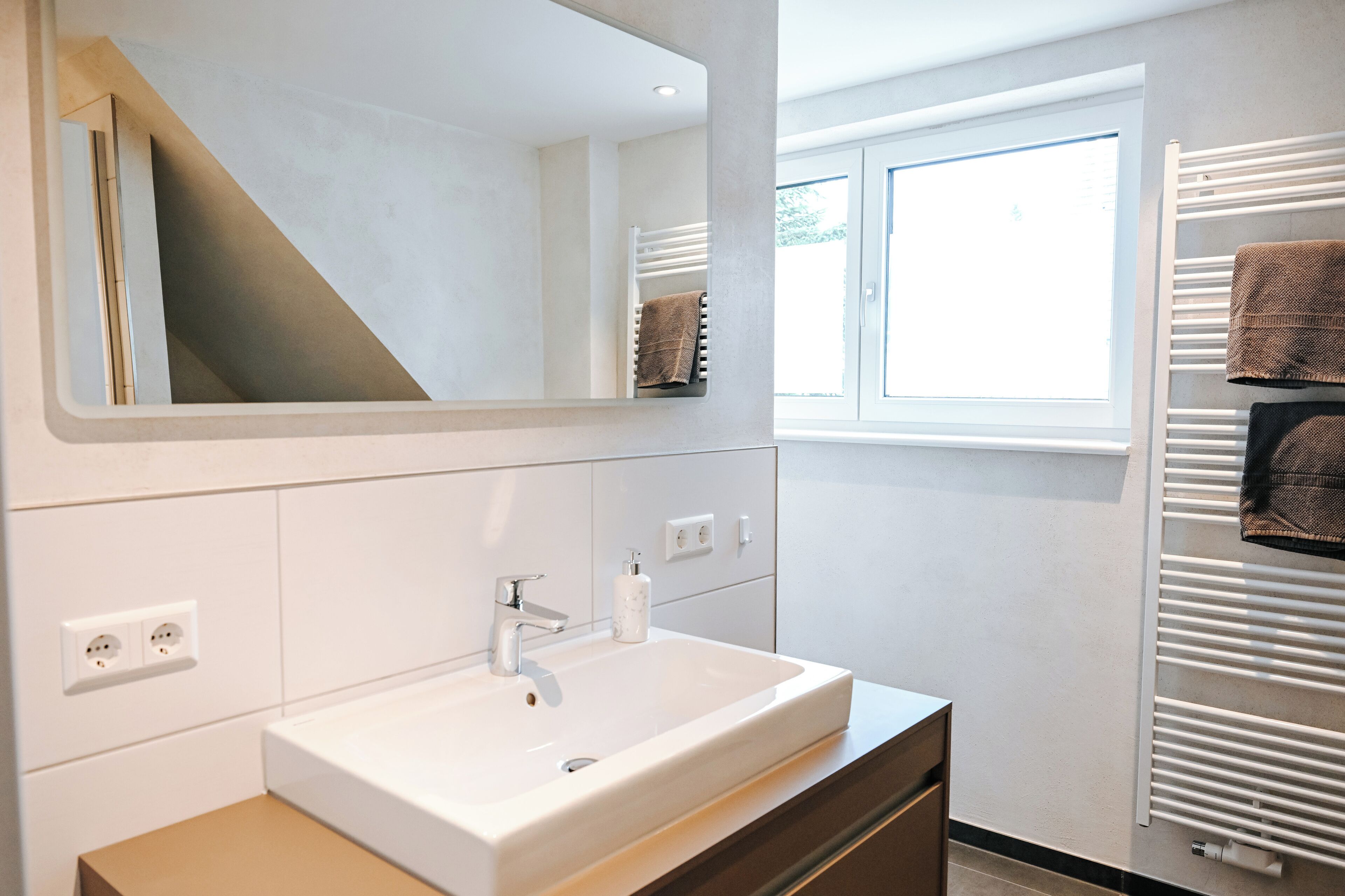 A modern bathroom with a large mirror, white sink, and towel racks.