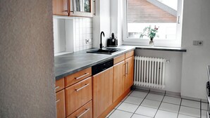 Eine Küche mit Holzschränken, einem schwarzen Spülbecken und einem Fenster mit Blick auf ein Haus.