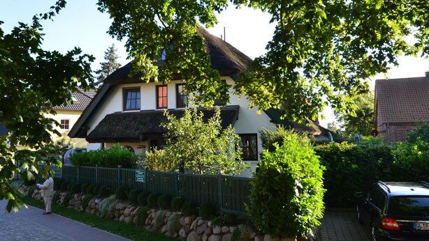 Ein traditionelles Haus mit Strohdach, umgeben von üppiger Vegetation und einer Steinmauer.