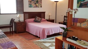 A bedroom with a bed, bedside tables, a desk, a chair, a bookshelf, and a window with shutters.