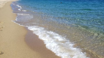 Ein Strand mit klarem Wasser, sandigem Ufer und blauem Himmel.