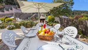 Un área de comedor al aire libre con una mesa preparada para dos, una cesta de mimbre con fruta y una copa de vino.