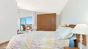 Un dormitorio con cama, mesita de noche, lámpara, armario y vistas al exterior a través de una puerta corrediza.