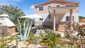 Una casa de dos pisos con un patio, un muro de piedra y un jardín con diversas plantas.