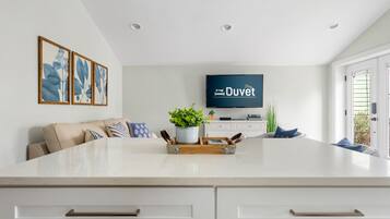 Una cocina moderna con una isla central, muebles blancos y un televisor de pantalla plana montado en la pared.