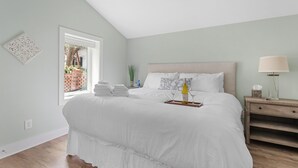 Une chambre avec un grand lit, une table de chevet, une fenêtre donnant sur un mur de briques et des plantes, et un luminaire au plafond.
