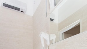 Une salle de bain avec des toilettes blanches, une étagère en verre, un lavabo blanc et une bouteille rouge de savon liquide.