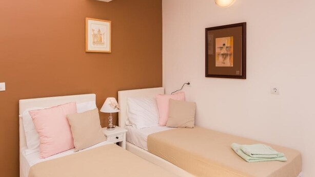 Une chambre avec deux lits, une table de chevet, une lampe fixée au mur et deux tableaux encadrés.