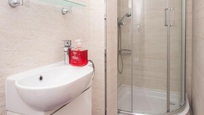 Une salle de bain moderne avec une douche à parois de verre, un lavabo blanc et une serviette violette sur le sol.