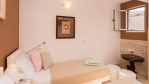 Une chambre à coucher avec un lit, une table de chevet, une petite table ornée de fleurs, un tableau encadré accroché au mur et une fenêtre dont le store est ouvert.